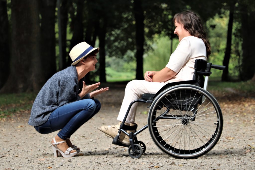 Woman on wheelchair smiling to woman with hat in a forest
